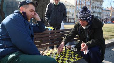 Para pria bermain catur di bangku kawasan pusat pejalan kaki di Kota Lviv, Ukraina, 20 Maret 2022. Lviv -- hanya 70 kilometer (45 mil) dari perbatasan Polandia -- sebagian besar telah terhindar dari kekerasan sejak Rusia melancarkan invasi militernya pada 24 Februari. (Alexey Filippov/AFP)