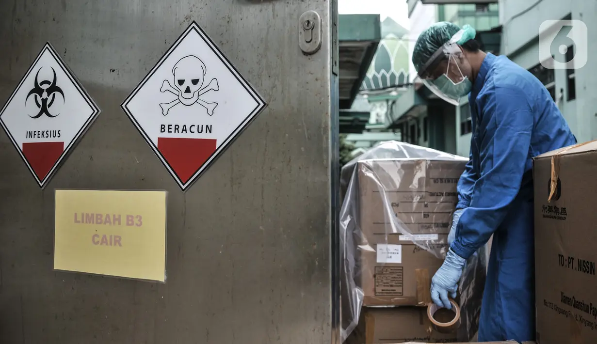 Petugas berpakaian APD mengemas limbah Covid-19 ke dalam kardus berlapis plastik di Tempat Penyimpanan Sementara Limbah B3 di Labkesda DKI Jakarta, Selasa (4/8/2020). Setiap kantong berisi limbah Covid-19 dibawa ke ruang sterilisasi sebelum diangkut ke tempat pembuangan. (merdeka.com/Iqbal Nugroho)