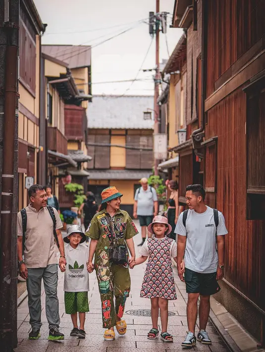 Potret gemas Ashanty bergandengan tangan dengan Anang dan ketiga anaknya. Ashanty mengenakan jumpsuit hijau bermotif ramai, bucket hat berwarna oranye, dan sandal kuning. Foto: Instagram.