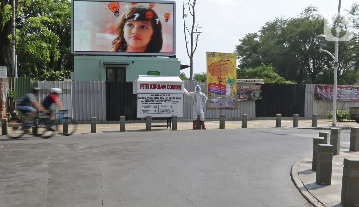 Pesepeda melintas di depan seni instalasi yang menggambarkan tenaga medis memegang peti jenazah korban COVID-19 di Kemang 1, Jakarta Selatan, Minggu (16/8/2020). Seni instalasi itu dipajang guna memberi peringatan kepada warga untuk tetap waspada terhadap COVID-19. (Liputan6.com/Herman Zakharia)