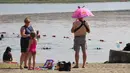 Seorang pria menggunakan payung melindungi kepala dan anak yang dipegangnya dari matahari di Goose Lake di Anchorage, Alaska (5/7/2019). Cuaca panas diperkirakan akan berlanjut hingga minggu depan. (AP Photo/Mark Thiessen)