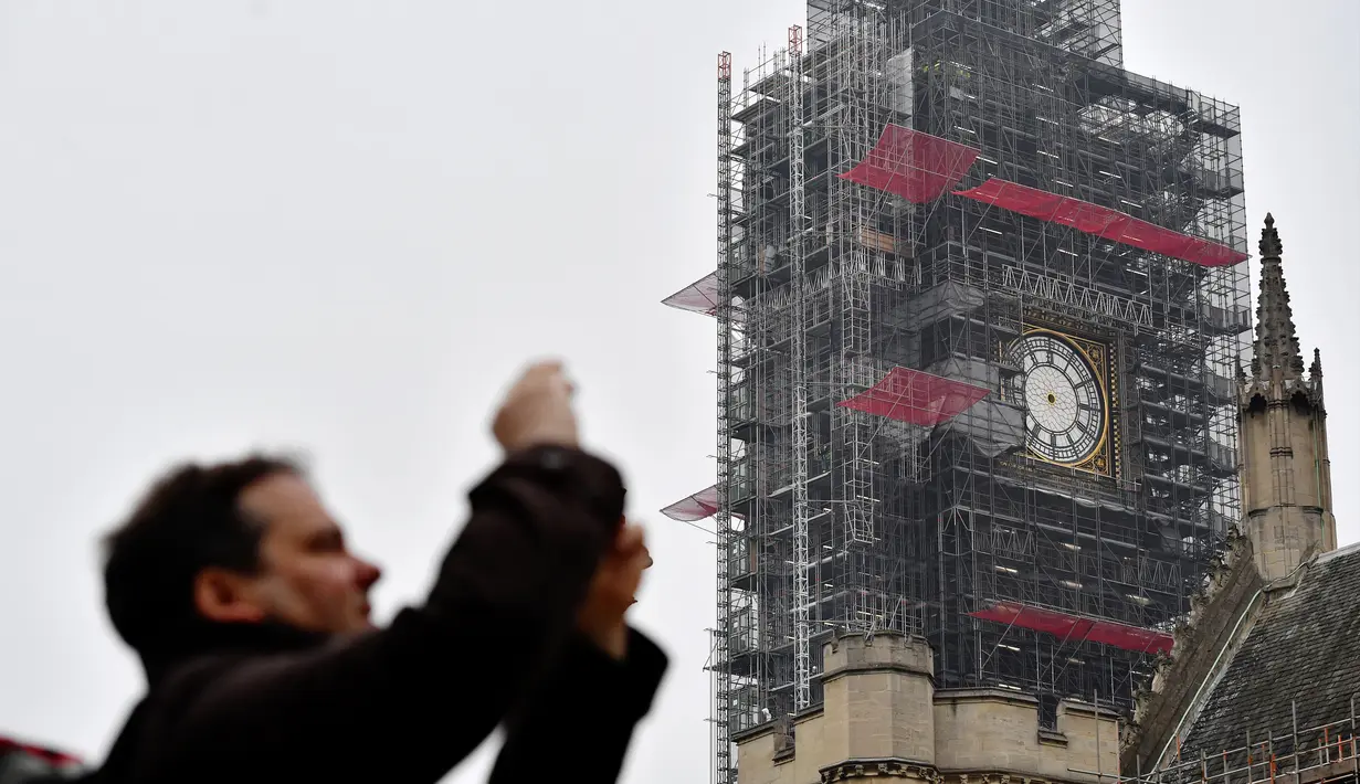 Seorang pria mengambil gambar dengan latar belakang jam Big Ben yang tidak ada jarumnya karena sedang dilakukan perbaikan dan pembersihan di London, Inggris (12/4). (AFP Photo/Ben Stansall)