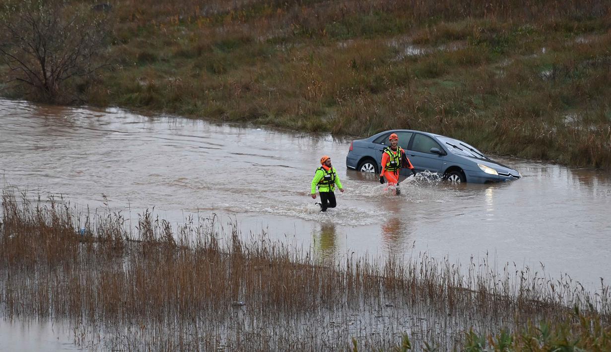Luapan sungai Herault diperkirakan akan menyebabkan beberapa kerusakan signifikan. Tampak dalam foto, petugas penyelamat berjalan melewati sebuah mobil di sepanjang sungai Herault yang meluap setelah hujan lebat di Agde, Prancis selatan pada Selasa 23 Desember 2025. (Sylvain THOMAS/AFP)