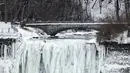Dua orang turis berjalan di depan Air Terjun Niagara, Ontario, Kanada, Senin (9/1). Amerika utara dan Kanada kini sedang terjadi penurunan temperatur sehingga membuat wilayah tersebut terkena cuaca dingin ekstrem. (Geoff Robins/AFP)