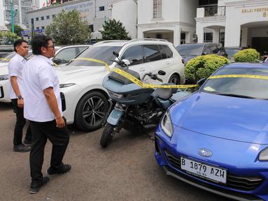 Petugas kepolisian memeriksa mobil sitaan terkait kasus situs judi online yang terparkir di Polda Metro Jaya, Jakarta, Senin (25/11/2024). (Liputan6.com/Herman Zakharia)