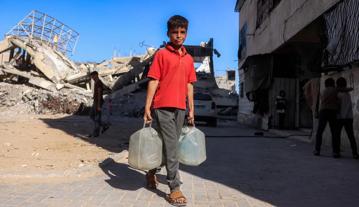 Seorang anak laki-laki berjalan membawa wadah air setelah mengisi ulang air dari sebuah tangki di kamp penampungan, Khan Yunis, Jalur Gaza Selatan pada 6 Juni 2026. (Bashar Taleb/AFP)