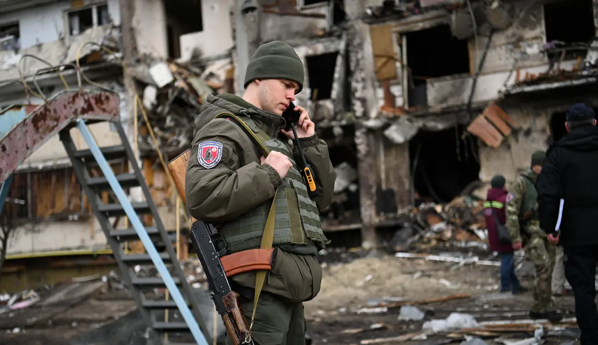 Seorang prajurit Ukraina berbicara di telepon di depan sebuah bangunan tempat tinggal yang rusak puing setelah peluru militer Rusia menghantam bangunan di Koshytsa Street, Kiev, Ukraina (25/2/2022). (AFP/Daniel Leal)