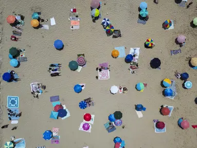 Foto udara menunjukkan orang-orang berjemur di pantai Costa da Caparica di Almada, dekat Lisbon, selama gelombang panas pertama tahun ini, pada tanggal 29 Juni 2025. (CARLOS COSTA/AFP)