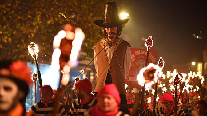 Peserta mengarak patung Guy Fawkes dalam perayaan Bonfire Night melintasi jalan di Sussex Timur, Inggris, Selasa (5/11/2019). Penduduk Inggris juga membawa patung berukuran besar dan mengaraknya sembari berparade. (Ben STANSALL/AFP)