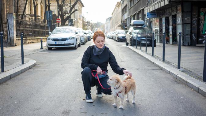 Andra Aron (32) berpose dengan anjingnya Gerald (4) saat perjalanan di Bucharest (28/3/2020). Undang-undang militer, yang disahkan pemerintah Rumania untuk mengurangi penyebaran virus corona, menyatakan berjalan bersama anjing adalah salah satu  kegiatan yang masih diizinkan. (AFP/Andrei Pungovschi)