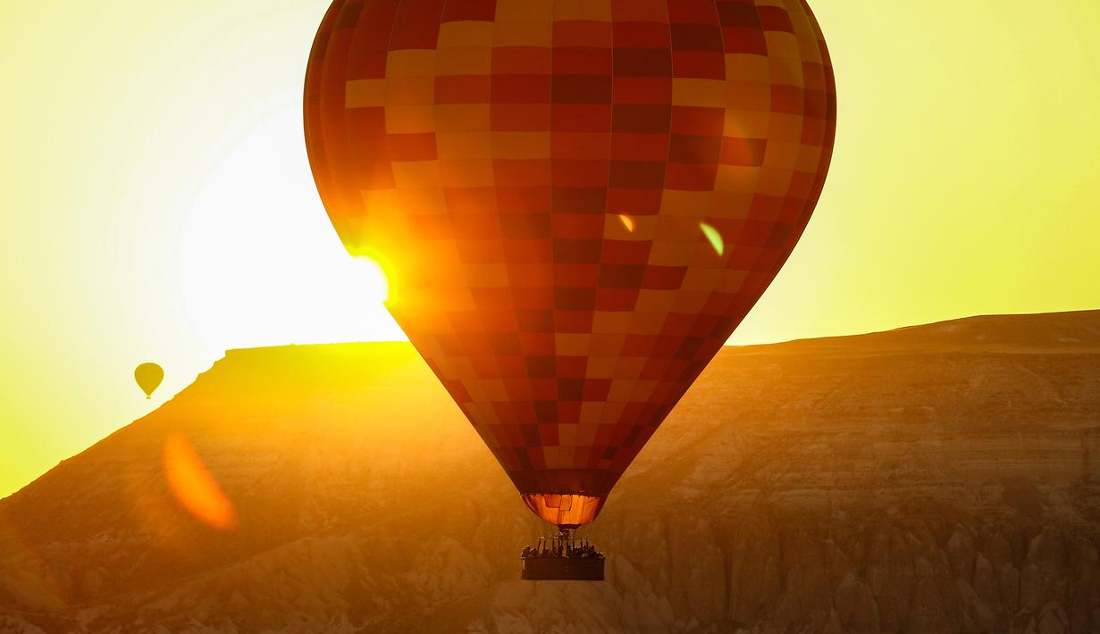 Para turis menaiki balon udara sambil menikmati matahari terbit di Kapadokia, Turki, Selasa (7/8). Cerobong Peri Kapadokia adalah lansekap batu vulkanik berbentuk kerucut yang menjulang tinggi ke langit. (AP Photo/Emrah Gurel)