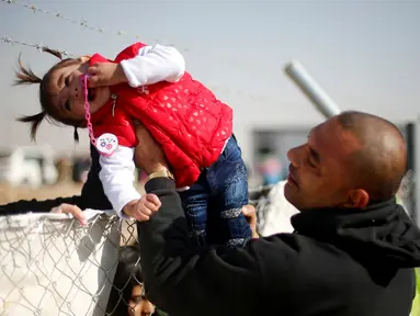 Seorang pria menyeberangkan anak perempuan melewati kawat berduri di kamp pengungsian Khazer, Irak (28/11). Mereka pergi meninggalkan daerah yang sebelumnya dikuasai kelompok militan ISIS untuk mengungsi ke tempat yang lebih aman. (Reuters/Mohammed Salem)