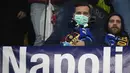 Seorang suporter Napoli  mengenakan masker menunggu dimulainya pertandingan antara Napoli dan Barcelona di Stadion San Paolo di Naples, Italia, Selasa, (25/2/2020). Dalam laga ini, Barcelona berhasil menanhan tuan rumah Napoli 1-1. (AFP Photo/Filippo Monteforte)