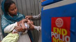 Seorang petugas kesehatan memberikan tetes vaksin polio kepada seorang anak saat kampanye vaksinasi polio dari rumah ke rumah di sebuah kawasan kumuh di Lahore, Paksistan, Senin (23/5/2022). Pakistan meluncurkan upaya anti-polio baru pada hari Senin, lebih dari seminggu setelah pejabat mendeteksi kasus ketiga tahun ini di wilayah barat laut negara itu yang berbatasan dengan Afghanistan. (Arif ALI / AFP)