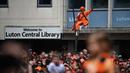 Seorang pendukung Luton Town menyambut kedatangan parade bus timnya melewati jalanan di Luton, Inggris setelah berhasil promosi ke Liga Inggris musim 2023/2024 pada Senin (29/05/2023) waktu setempat. The Hatters sukses menyegel tiket promosi setelah memenangkan laga play-off divisi Championship melawan Covetry City 6-5 melalui adu penalti di Wembley, Sabtu (27/5/2023). (AFP/Daniel Leal)