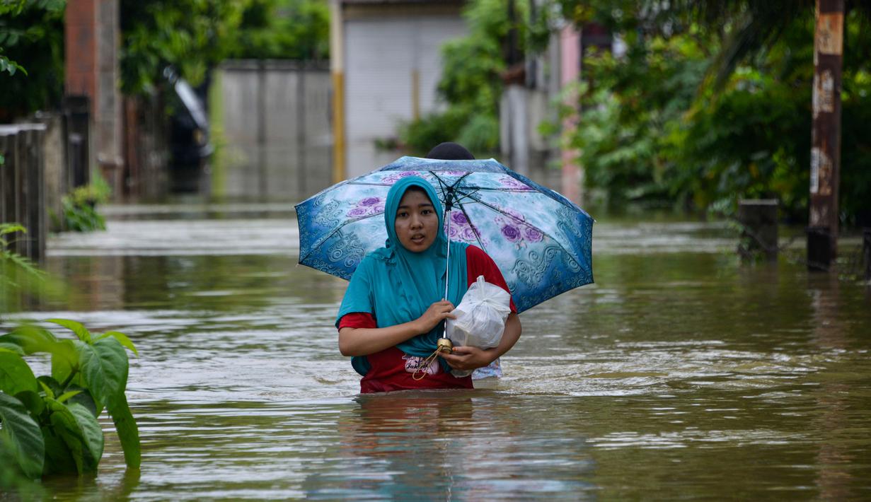Seorang perempuan melintasi lingkungan yang banjir setelah tiga hari diguyur hujan lebat di Banda Aceh, Aceh, Sabtu (9/5/2020). Banjir akibat intensitas hujan tinggi tersebut mengakibatkan sebagian besar kawasan di ibu kota Provinsi Aceh ini digenangi air. (Photo by CHAIDEER MAHYUDDIN/AFP)
