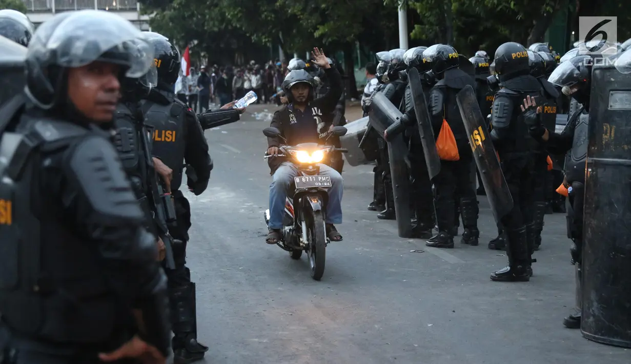 Pengendara melintas di antara polisi yang berjaga di sekitaran Stasiun Palmerah, Jakarta, Senin (30/9/2019). Jalur di kawasan itu telah dibuka, namun kendaraan harus berhati-hati karena banyaknya batu sisa bentrokan massa di belakang gedung DPR yang berakhir ricuh. (Liputan6.com/Angga Yuniar)