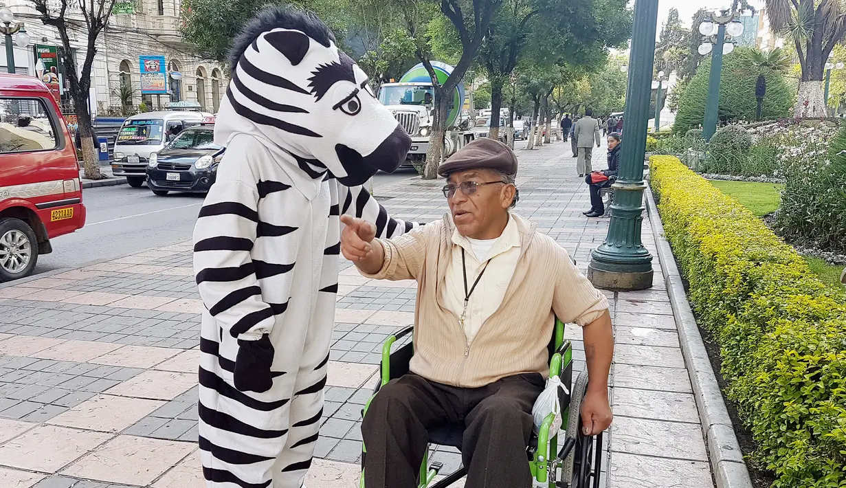 Warga berpakaian seperti zebra berbincang dengan seorang kakek penyandang disabilitas saat program pendidikan di jalan di La Paz, Bolivia,(5/12). (REUTERS/David Mercado)