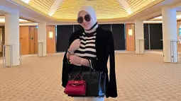 Syahrini mengunggah foto saat berada di Singapura. Dia mengenakan outfit berwarna hitam putih dan menutupi bagian perutnya dengan dua buah tas. (foto: Instagram/ princessyahrini)