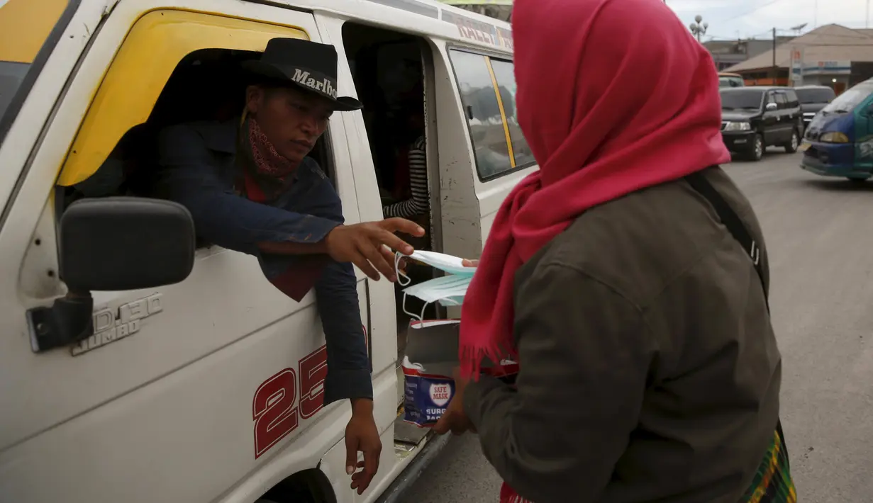 Seorang warga menerima masker yang dibagikan para relawan di kawasan Berastagi, Karo, Sumatera Utara, 25 Juni 2015. Debu vulkanik akibat erupsi Gunung Sinabung masih menutupi sebagian Kota Berastagi. (REUTERS/Beawiharta)