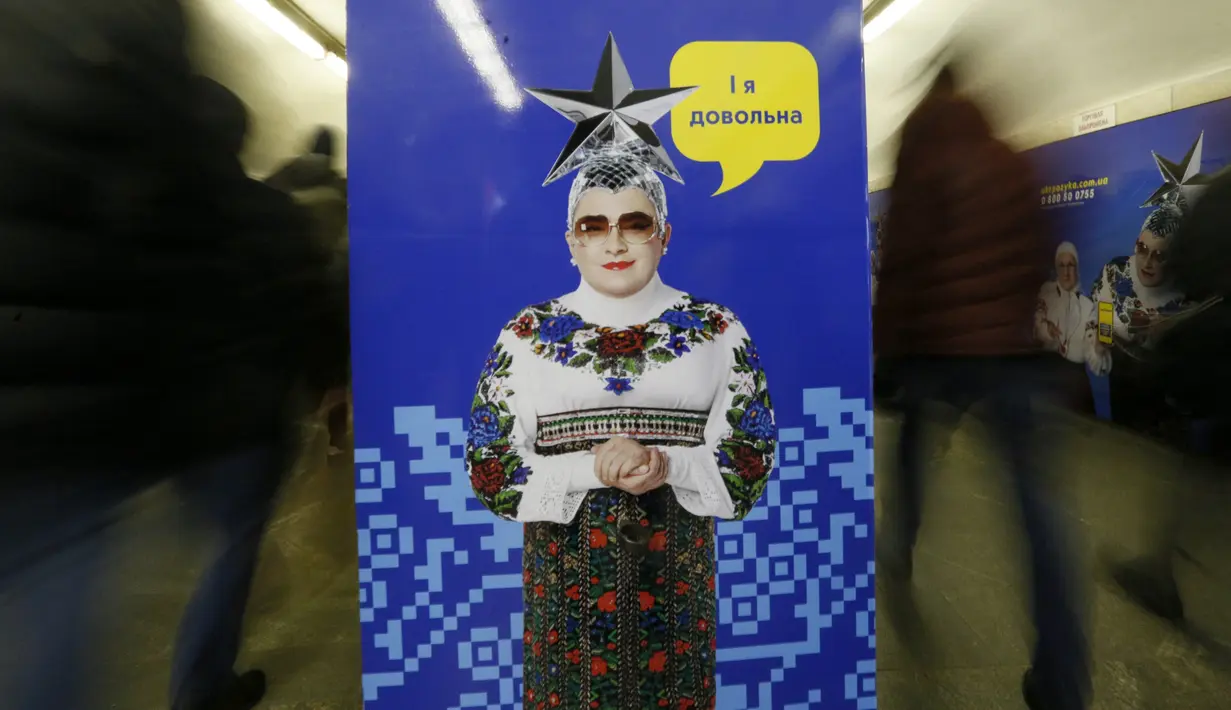 Sejumlah penumpang melewati poster yang menggambarkan penyanyi Ukraina Verka Serduchka dengan teks yang menyatakan "Aku bahagia", di stasiun metro bawah tanah kota di Kyiv, Ukraina, Rabu, (29/1/2020). (AP Photo / Efrem Lukatsky)