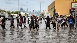 Pusat Meteorologi Nasional UEA telah mengeluarkan peringatan akan adanya hujan di seluruh negeri dari hari Kamis (18/12) sampai Jumat (19/12/2025), termasuk di Dubai dan ibu kota Abu Dhabi. Tampak dalam foto, para pria mengangkat ujung celana mereka untuk menyeberangi genangan air banjir saat melintasi jalan setelah hujan lebat, di Dubai, Uni Emirat Arab (UEA) pada Jumat 19 Desember 2025. (FADEL SENNA/AFP)