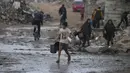 Diketahui, sekitar 85% infrastruktur air dan sanitasi di Gaza telah rusak atau hancur akibat serangan militer Israel dalam dua tahun terakhir. Tampak dalam foto, seorang anak laki-laki membawa dua ember kosong saat berjalan menuju tempat mengambil air di tengah hujan deras di kawasan Sheikh Radwan, Kota Gaza, Jumat 14 November 2025. (AP Photo/Jehad Alshrafi)