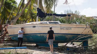 Dua orang pria berdiri dekat sebuah kapal yang terhempas ke daratan akibat terhempas badai Irma di Coconut Grove, Florida, Senin (11/9).Badai Irma menghantam negara bagian Florida dengan kecepatan angin mencapai 200 km/jam. (SAUL LOEB/AFP)