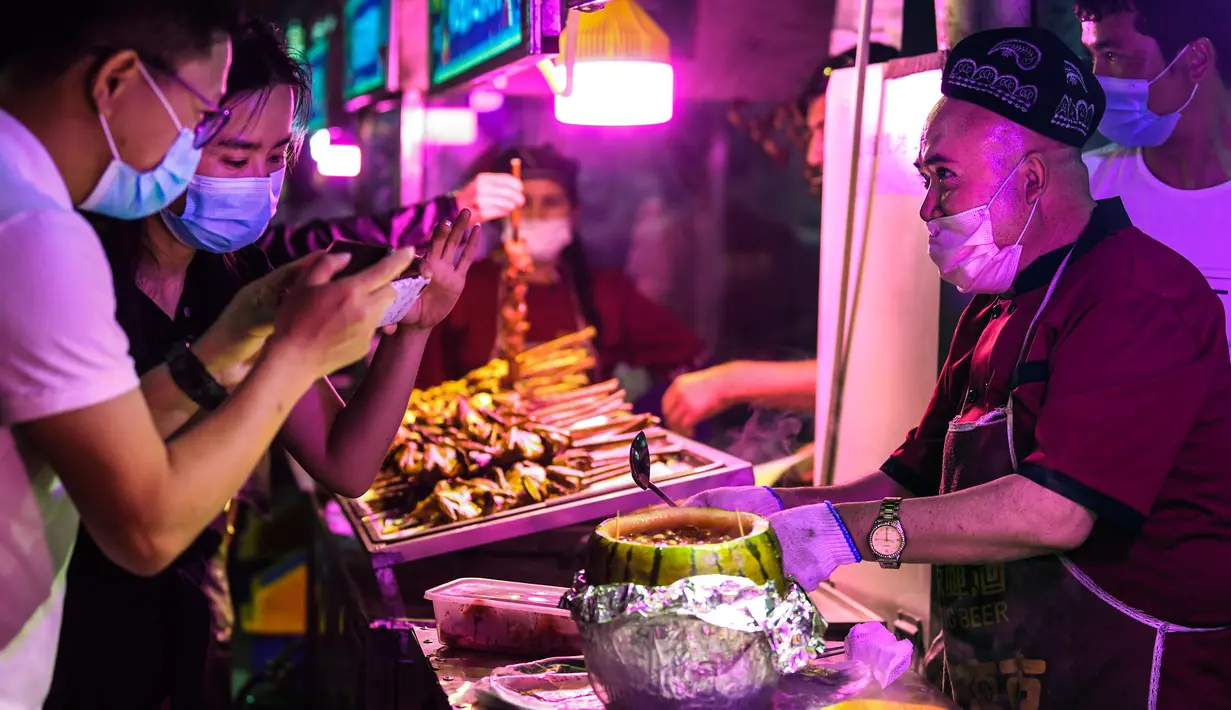 Seorang pedagang menyajikan hidangan lokal kepada para pelanggan di sebuah pasar malam di Hotan, Daerah Otonom Uighur Xinjiang, China barat laut, pada 18 Mei 2020. Seiring cuaca mulai menghangat, aktivitas pariwisata lokal pun perlahan kembali pulih. (Xinhua/Wang Fei)