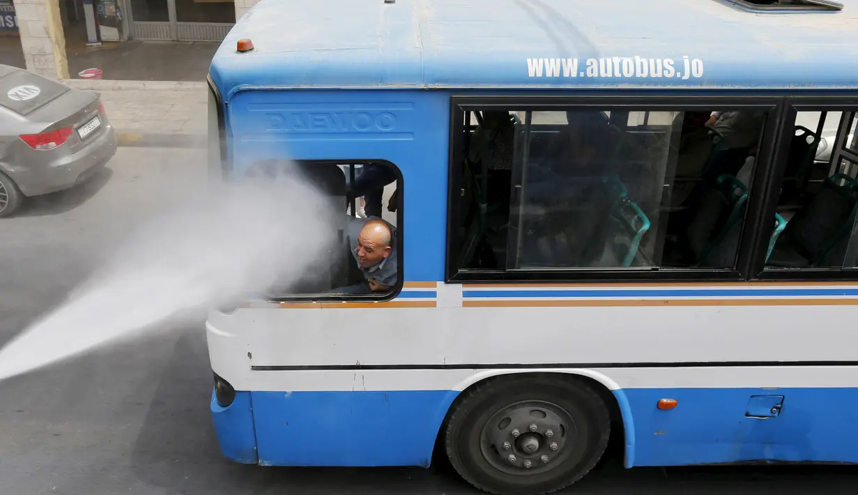 Seorang sopir bus disemprot oleh personel dinas Kota Amman menggunakan sprinkler air untuk mengurangi efek dari gelombang panas di Yordania, Senin(3/8/2015). (REUTERS/Muhammad Hamed)