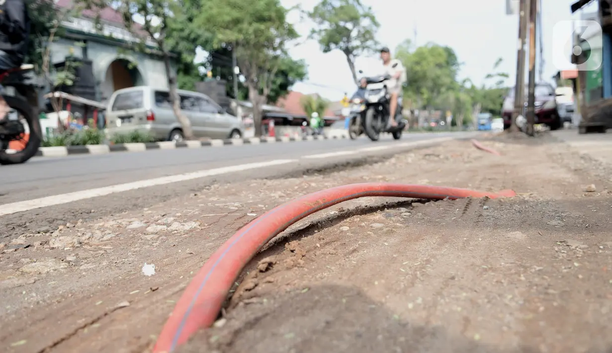 Kendaraan melintasi kabel proyek PLN yang terbengkalai di Jalan Jatinegara Kaum, Jakarta, Minggu (12/1/2020). Kurangnya pengawasan dalam penyelesaian proyek instalasi listrik bawah tanah PLN tersebut menyebabkan banyak kabel masih muncul di trotoar dan bahu jalan. (merdeka.com/Iqbal S. Nugroho)