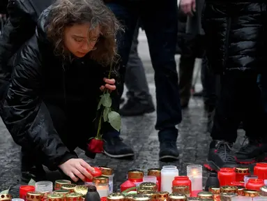 Seorang wanita muda meletakkan lilin dan bunga mawar di tugu peringatan sementara untuk para korban di luar Universitas Charles di pusat kota Praha, pada tanggal 22 Desember 2023. (Michal CIZEK/AFP)