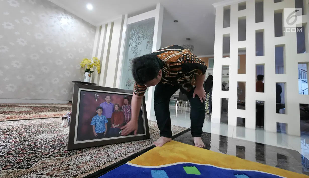 Muhammad Ivanka Rizaldi Nugroho membersihkan foto keluarga di rumah duka Raffles Hils, Depok, Jawa Barat, Minggu (7/7/2019). Rencananya jenazah Sutopo akan dimakamkan di Boyolali Jawa Tengah Senin (8-7-2019). (Liputan6.com/Herman Zakharia)