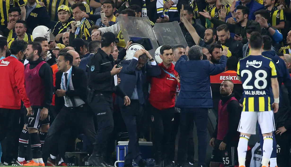Pelatih Besiktas, Senol Gunes memegangi kepalanya setelah terkena lemparan benda tajam dari tribun penonton pada semifinal Piala Turki melawan Fenerbahce di Istanbul, Kamis (19/4). Gunes harus dilarikan ke rumah sakit dan menerima lima jahitan. (AFP)