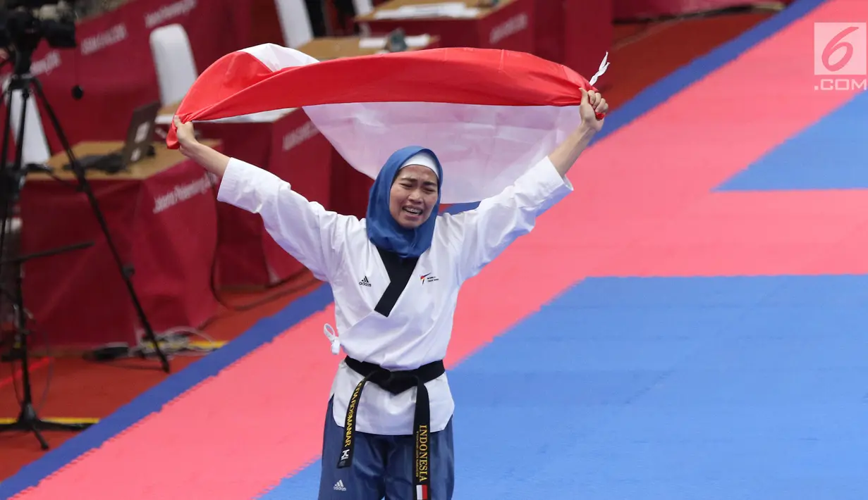 Atlet Taekwondo putri Indonesia, Defia Rosmaniar mengibarkan bendera Merah Putih saat merayakan kemenangan atas Salahshouri Marjan (Iran) pada Final Women Individual Poomsae di JCC, Jakarta, Minggu (19/8). (Liputan6.com/Helmi Fithriansyah)