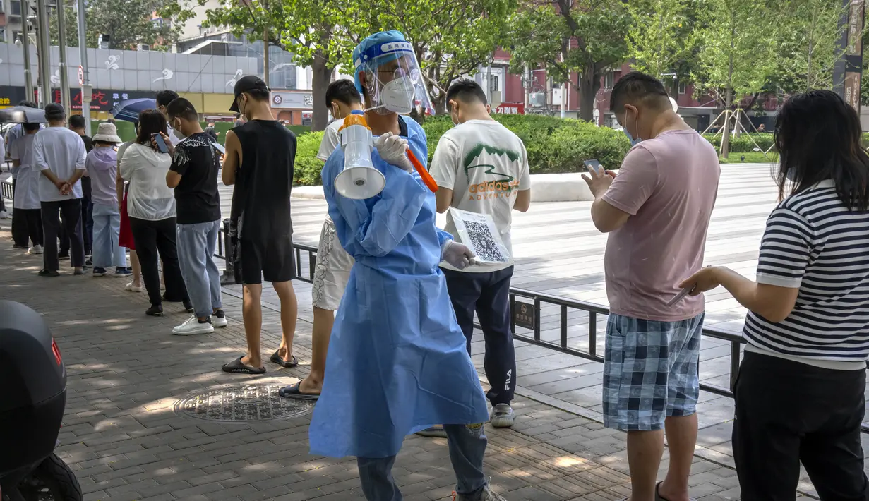 Seorang pekerja yang mengenakan pakaian pelindung dan membawa megafon memegang selembar dengan kode QR untuk orang-orang yang mengantre untuk tes virus corona COVID-19 di tempat pengujian pada hari ketiga pengujian massal untuk jutaan penduduk di Distrik Chaoyang, Beijing, China, 15 Juni 2022. (AP Photo/Mark Schiefelbein)