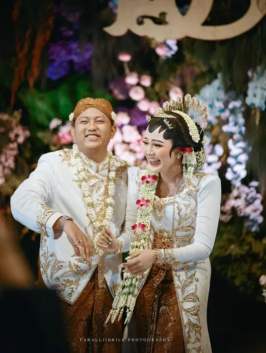 Bella Bonita tampak tak mengenakan banyak aksesori lain yang berlebihan. Ia tampak hanya mengenakan anting dan memadukan penampilannya dengan kain batik bernuansa emas sebagai bawahan, yang juga serasi dengan milik Denny Caknan. Foto: Instagram.