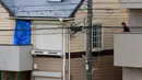 Seorang pria berada di samping rumah yang ditutupi kain biru di mana polisi menemukan sembilan mayat termasuk dua kepala yang disimpan di kotak pendingin di Zama, Prefektur Kanagawa, Jepang, (31/10). (AFP Photo/Toru Yamanaka)