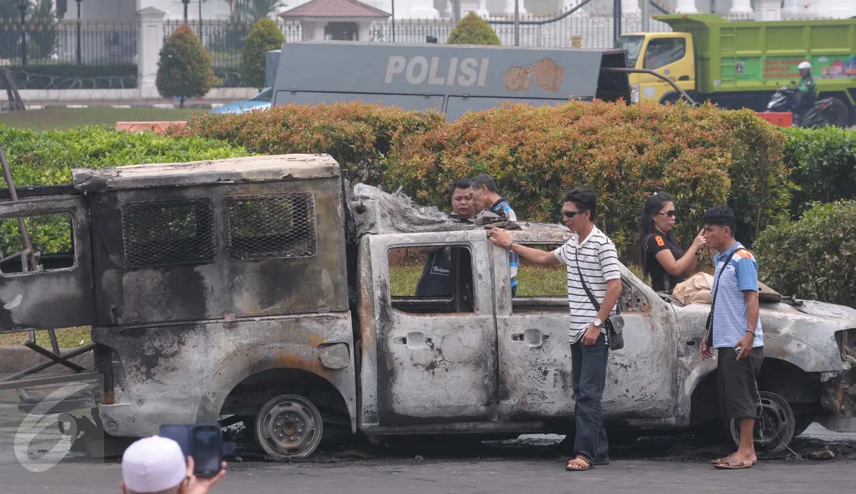 Sejumlah warga berfoto di dekat bangkai mobil yang dibakar demonstran 4 November di kawasan Monas, Jakarta, Sabtu (5/11). Pengunjung menjadikan dua kendaraan milik kepolisian tersebut sebagai objek foto dan melakukan swafoto. (Liputan6.com/Angga Yuniar)