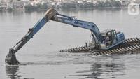Pekerja menggunakan beko mengeruk lumpur yang mengendap di Waduk Pluit, Senin (13/6/2022). Pengerukan lumpur rutin ini dilakukan sebagai upaya mengurangi endapan serta tanaman liar dan mencegah banjir di kawasan tersebut. (merdeka.com/Iqbal S Nugroho)