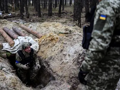 Seorang anggota tentara Ukraina memeriksa sebuah parit di base camp Rusia yang kosong di dekat Buda-Babynetska, utara Kiev, pada 5 April 2022, beberapa hari setelah pasukan Rusia mundur. (RONALDO SCHEMIDT / AFP)