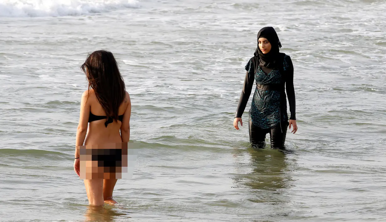 Seorang wanita mengenakan burkini di Laut Mediterania, Tel Aviv, Israel (30/8). Para wanita hijab ini tetap santai di tengah keramaian wanita berbikini. (REUTERS / Baz Ratner)