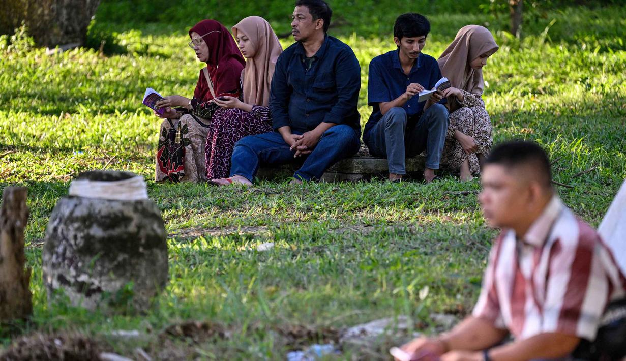 Orang-orang berdoa untuk kerabat mereka yang meninggal dunia dalam peristiwa gempa dan tsunami Aceh pada 2004 lalu di sebuah kuburan massal di Siron, pada 26 Desember 2025. Hari ini, Jumat (26/12/2025), peringatan 21 tahun tragedi gempa dan tsunami Aceh 2004 tetap digelar. (CHAIDEER MAHYUDDIN/AFP)