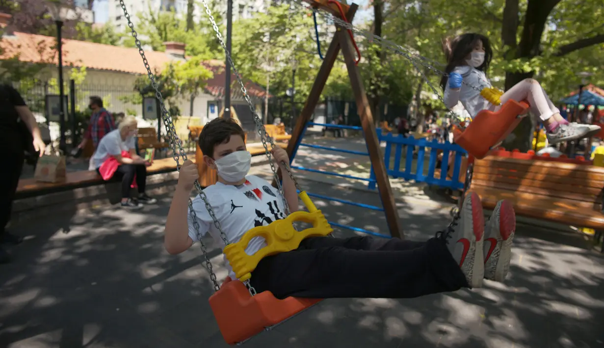 Anak-anak dengan mengenakan masker bermain ayunan di taman umum Kugulu, di Ankara, Rabu (13/5/2020). Turki mengizinkan anak-anak berusia 14 tahun ke bawah untuk meninggalkan rumah pertama kalinya dalam 40 hari sebagai bagian dari rencana normalisasi COVID-19 di negara tersebut. (AP/Burhan Ozbilici)