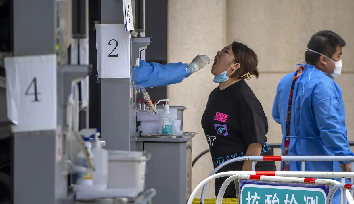 Pekerja menyeka tenggorokan seorang wanita di tempat pengujian virus corona COVID-19 pada hari ketiga tes massal untuk jutaan penduduk di Distrik Chaoyang, Beijing, China, 15 Juni 2022. (AP Photo/Mark Schiefelbein)