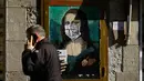 Seorang pria melewati poster seniman Italia TVBOY bergambar Mona Lisa karya Leonardo da Vinci mengenakan masker dan memegang smartphone di Barcelona, Selasa (18/2/2020). Instalasi muncul setelah Mobile World Congress (MWC) 2020 batal digelar karena wabah virus corona yang mencekam. (PAU BARRENA/AFP)