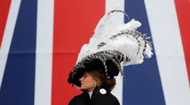 Seorang wanita mengenakan topi atau fascinator unik bermotif bulu melintas di depan bendera Union Jack saat menghadiri ajang pacuan kuda Royal Ascot di Ascot, Inggris, Selasa (18/6/2019). Royal Ascot menjadi ajang bagi wanita Inggris untuk tampil dengan fascinator unik. (AP Photo/Alastair Grant)