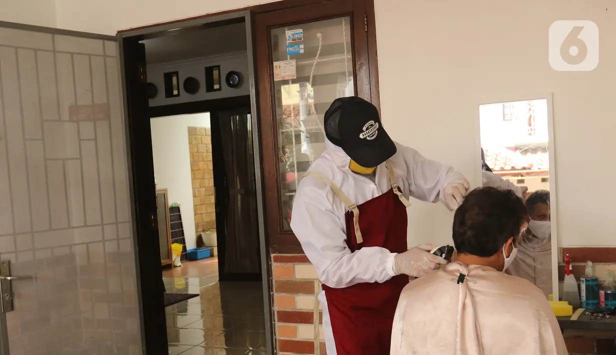 Tukang cukur mengenakan APD saat memotong rambut di halaman rumah pelanggan, Kelapa Dua, Depok, Jawa Barat, Senin (27/4/2020). Penerapan PSBB Kota Depok membuat tukang cukur tersebut menerima jasa panggilan ke rumah dan mengenakan APD untuk mencegah penularan COVID-19. (Liputan6.com/Herman Zakharia)