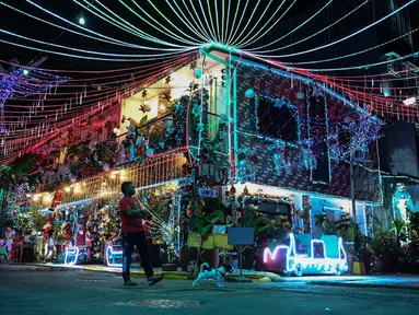 Seorang pria berjalan dengan seekor anjing melewati sebuah rumah bertema Natal di Manila, Filipina (21/12/2022). Perayaan Natal tinggal menghitung hari, warga Manila antusias mengunjungi rumah yang didekor dengan ornamen dan hiasan Natal itu. (AFP/Jam Sta Rosa)