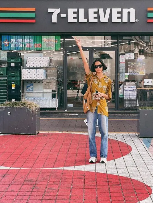 Berpose di depan 7 Eleven, ia tampil bergaya vintage dengan memadukan atasan kuning, celana jeans, dan sneakers putih. Gayanya disempurnakan dengan totebag dan kacamata hitam.  (Instagram/putrimarino).